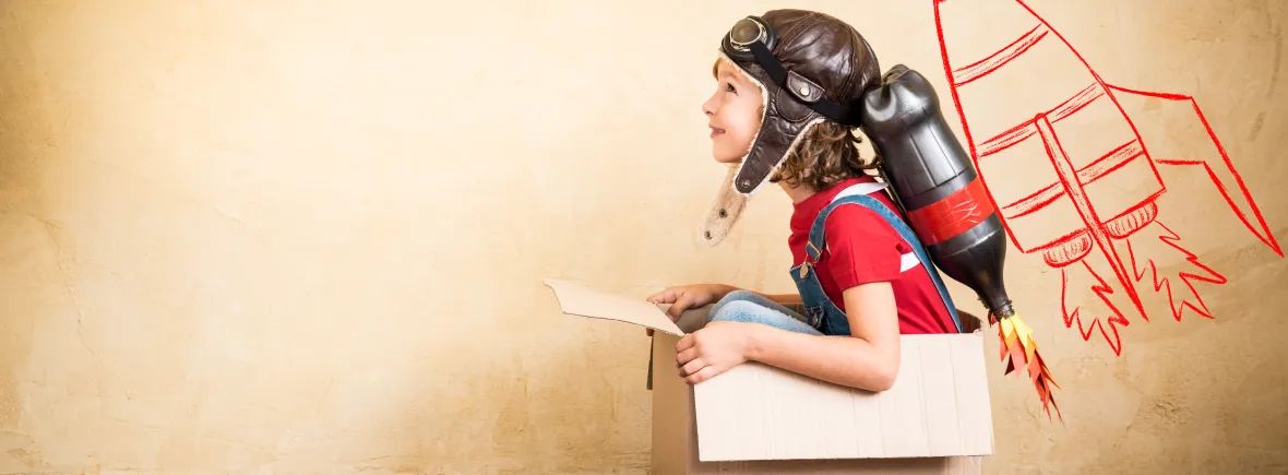A child in an aviator cap sitting in a cardboard box with a homemade rocket pack